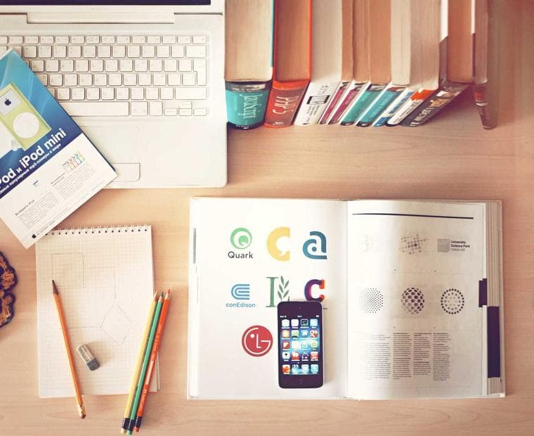 A desk from above: keyboard, open notebook, pens and coloured markers laid out in rows.