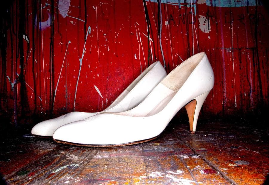 A pair of white heeled shoes standing against a red painted door.