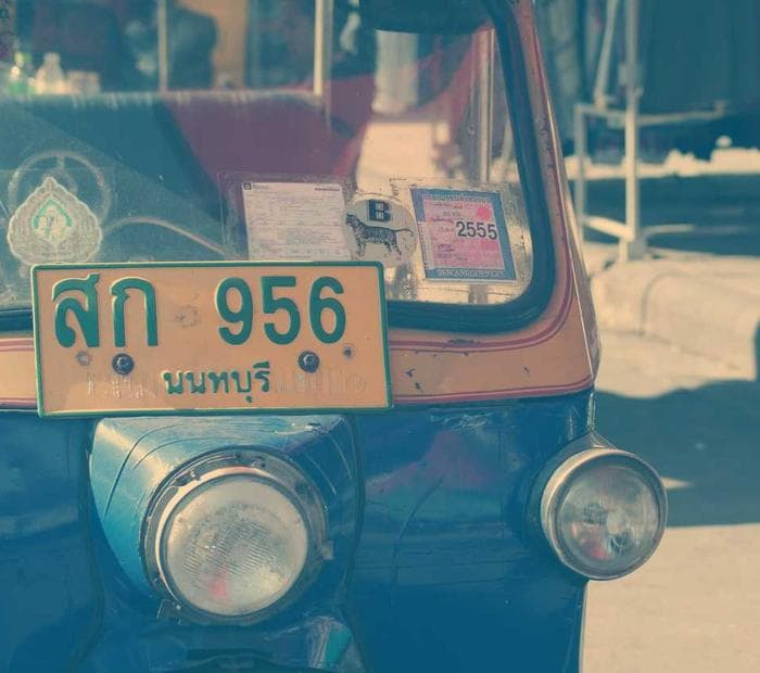The front of a three wheeled delivery vehicle, headlights and licence plate visible.